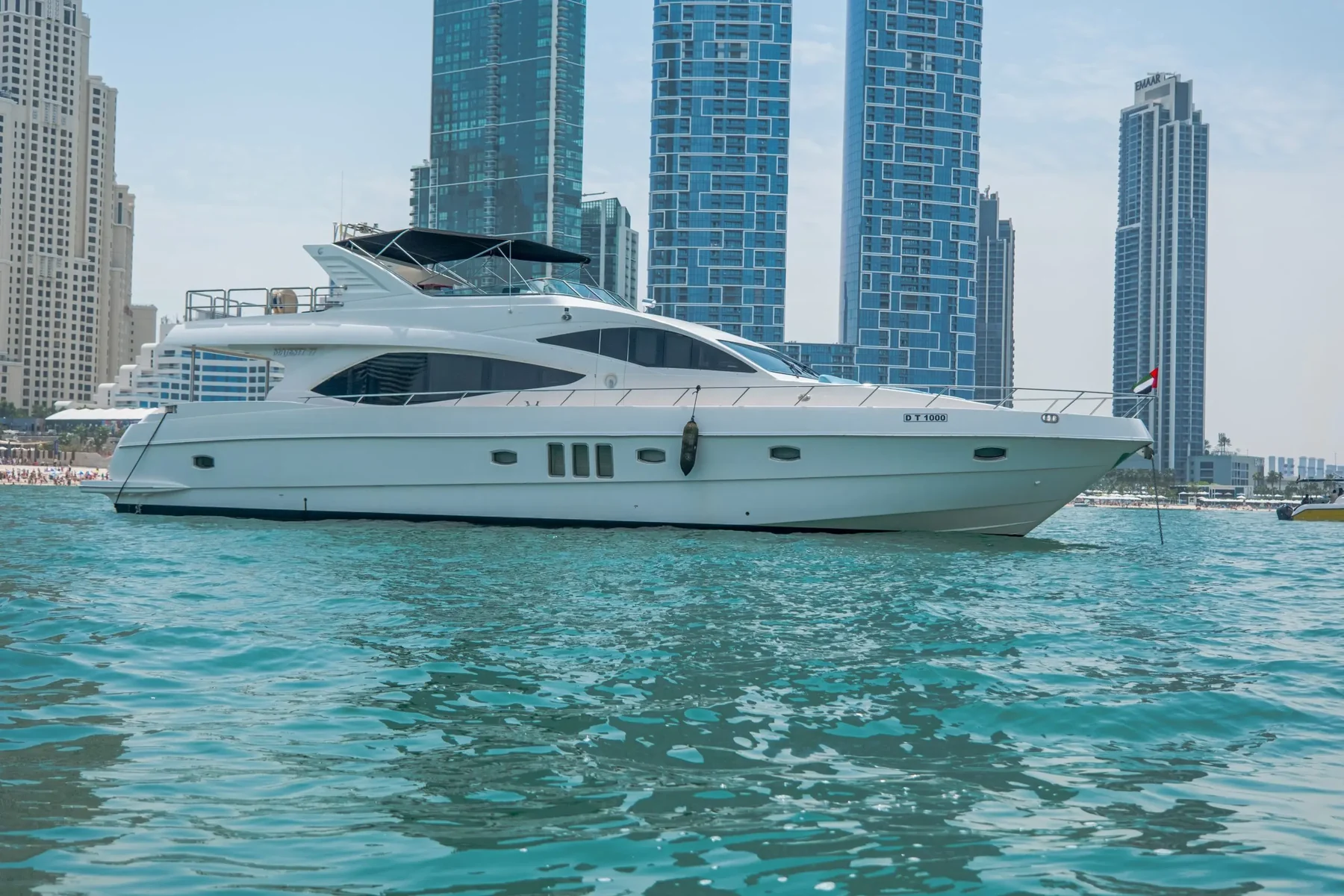 Long white three-deck superyacht anchored on turquoise water in front of the Dubai Marina towers